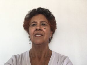 Foto de Elza Ambrosio, uma mulher negra, de cabelos curtos cacheados e em tor avermelhado. Ela olha para a direita com uma expressão contemplativa.