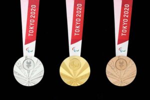 Foto das medalhas paralímpicas de Tóquio, com detalhes encravados em cada uma delas e uma faixa em braile. Da esqueda para a direita: prata, ouro e bronze.