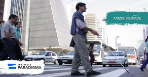 Homem surdocego com a bengala branca e vermelha, atravessando rua na faixa de pedestres. Texto: Acessibilidade.
