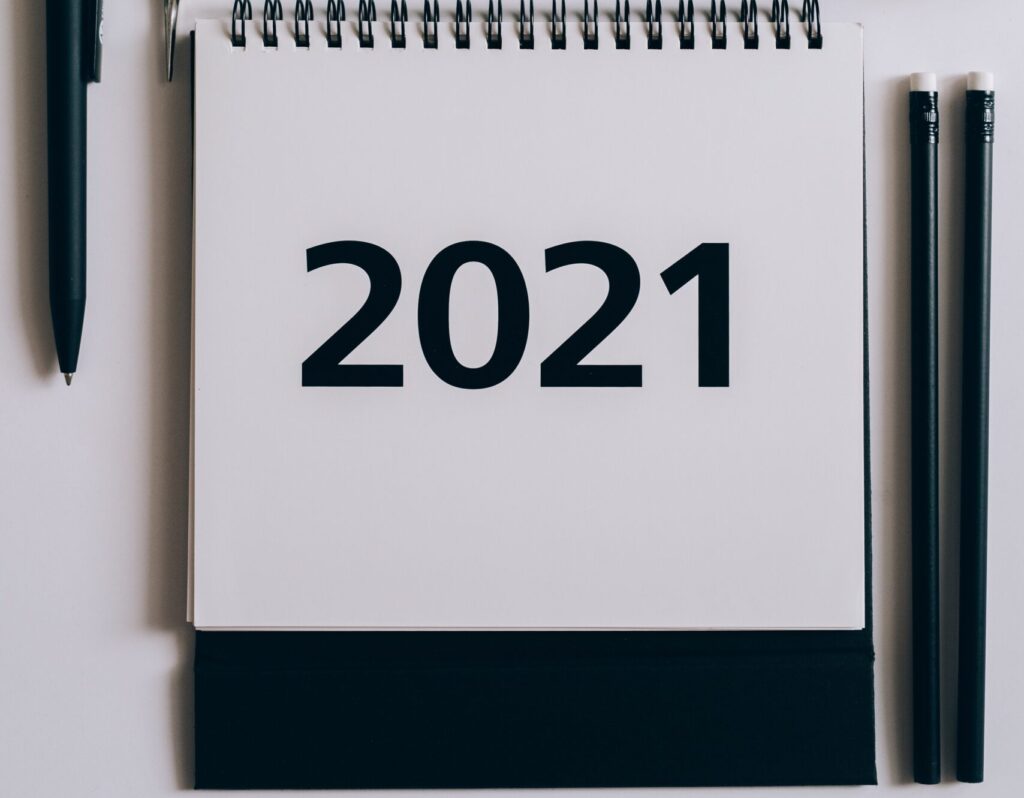 Foto de um calendário com a primeira folha escrita 2021. Do lado esquerdo do calendário, há uma caneta preta e, do lado direito, há dois lápis pretos