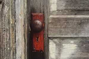 Foto em plano detalhe de uma maçaneta bola, bem antiga em uma porta de madeira