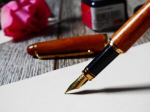 Foto em plano detalhe de uma caneta tinteiro sobre um papel branco em uma mesa de madeira