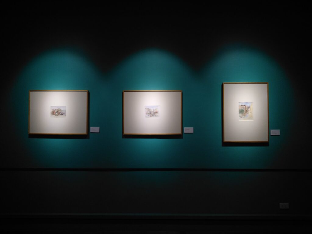 Em uma parede azul pretróleo, três quadros pendurados com spots de luz os iluminando